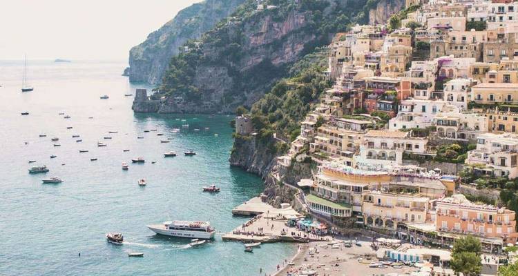 Cliff-side village cascading toward a turquoise bay dotted with boats along Italy’s Amalfi Coast.