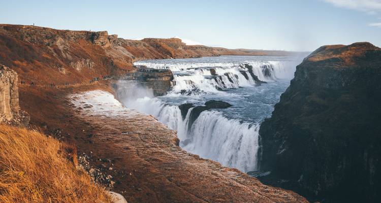 Gullfoss waterfall with mist rising and a rocky foreground.