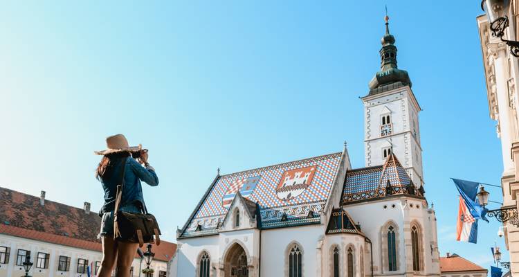 A person taking a photo of a historic church with colorful roof tiles.