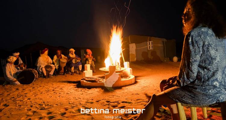 A group of people gathered around a fire with a visible watermark.