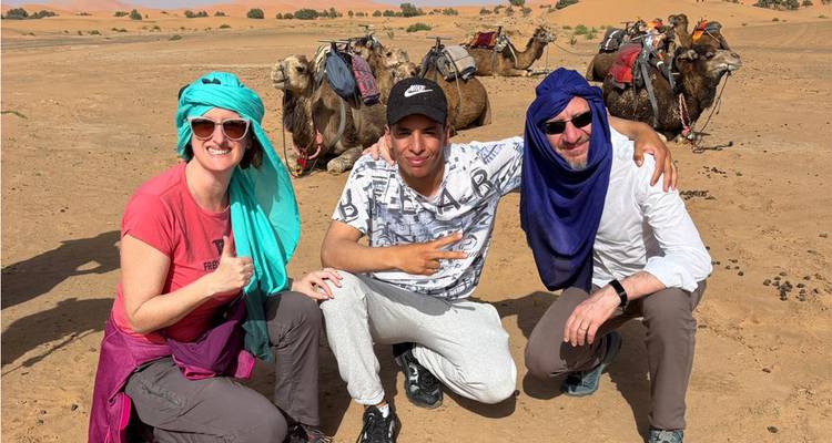 A group of people posed with camels in the desert.