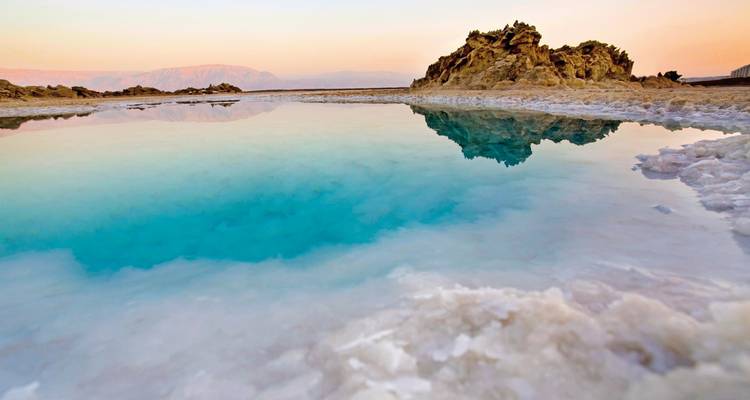 Turquoise waters at the Dead Sea bordered by rocky salt formations.
