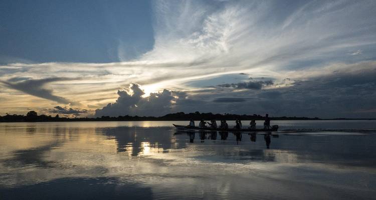 Silhouette of a canoe with people paddling on a calm lake during sunset.