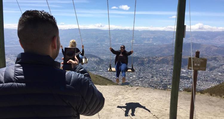 People on swings overlooking a city with mountains in the background.