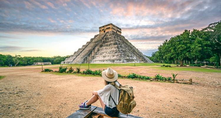 Tourist sitting in front of an ancient pyramid at sunset.