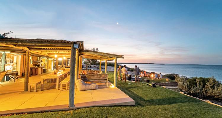 Des gens se détendant près d'un foyer au bord de la mer au coucher du soleil.
