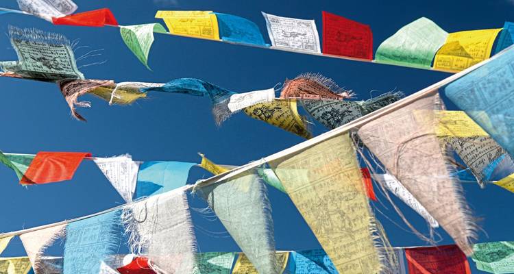 Des drapeaux de prière colorés tendus à travers un ciel bleu clair.