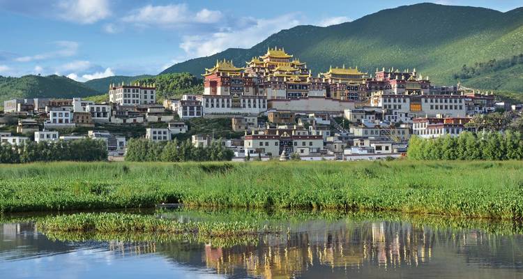 Complexe de temples de style tibétain traditionnel avec des montagnes en arrière-plan.