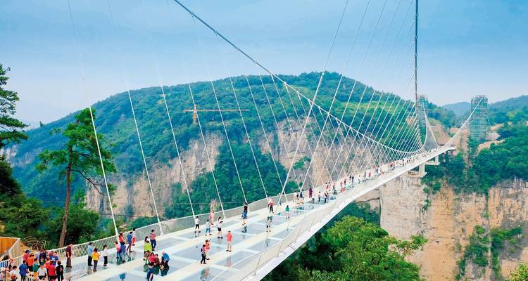 Glasbrücke mit Menschen und Bergen im Hintergrund.