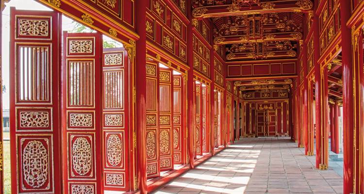 Un couloir avec des détails en bois rouge et or complexes et des fenêtres à treillis.