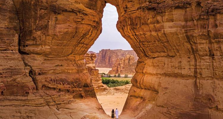 Un couple marchant à travers une arche rocheuse naturelle dans le désert.