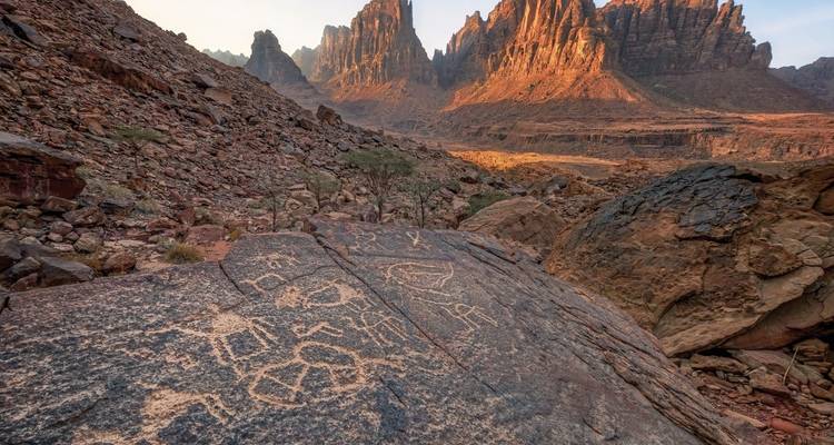 Pétroglyphes anciens sur un rocher avec des montagnes en arrière-plan.