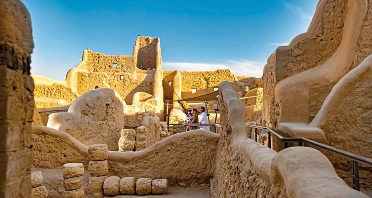 Personas explorando ruinas antiguas con paredes lisas de barro.