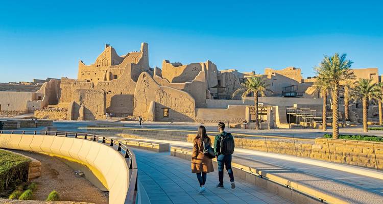 Walking path beside ancient ruins with people strolling.