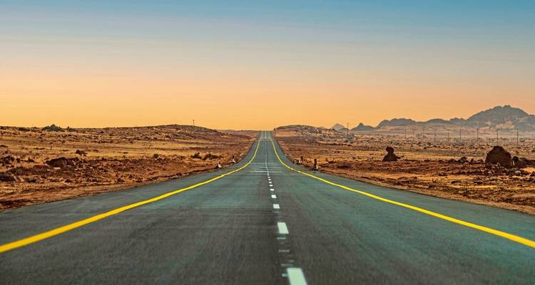 Long empty road through a desert landscape at sunset.