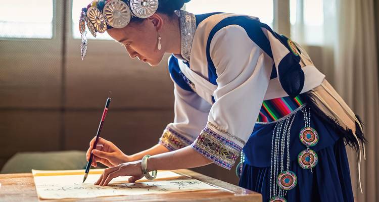 Femme en tenue traditionnelle pratiquant la calligraphie à l'intérieur.