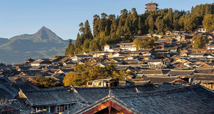 Vue d'une ville chinoise avec des toits traditionnels et des montagnes lointaines.