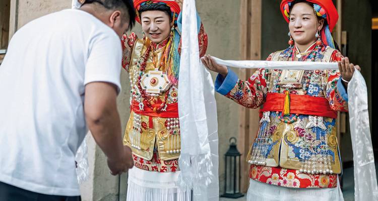 Cérémonie traditionnelle avec deux femmes en tenue colorée présentant une écharpe.