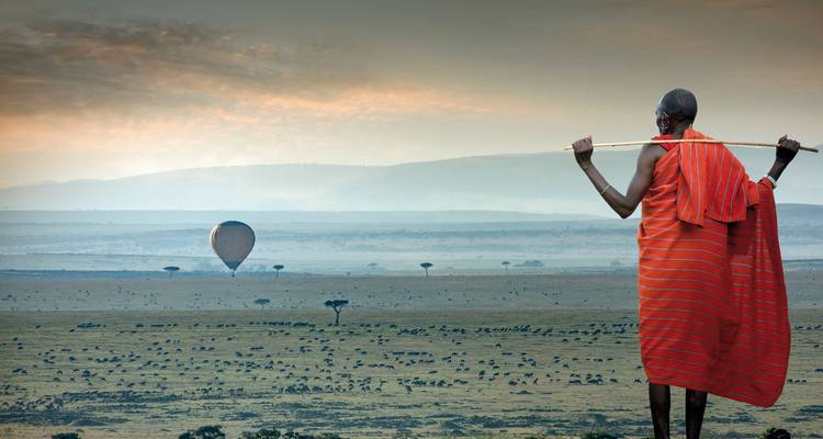 Personne tenant un bâton avec une montgolfière en arrière-plan.