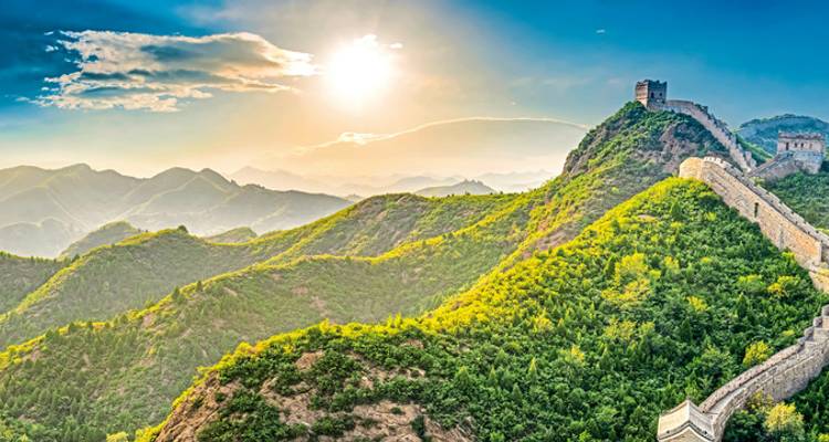 Chinesische Mauer, die sich bei Sonnenuntergang über üppige grüne Hügel erstreckt.