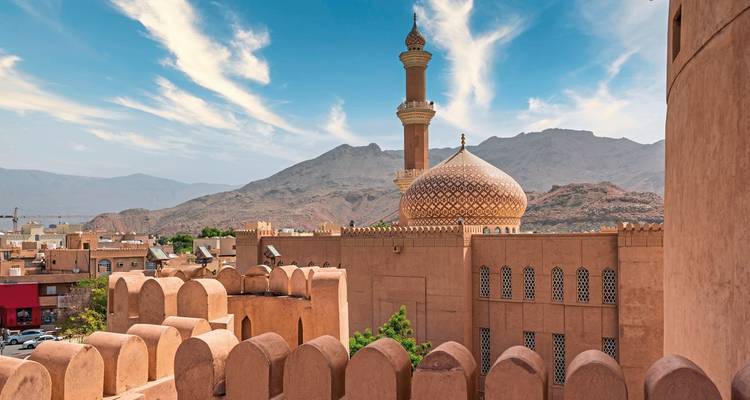 Une mosquée dans un paysage urbain avec des montagnes en arrière-plan et un ciel bleu dégagé.
