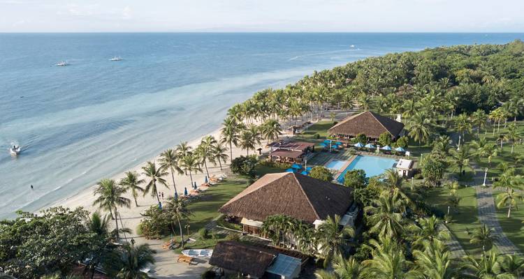 Luchtfoto van een tropisch strandresort met weelderig groen en een zwembad.