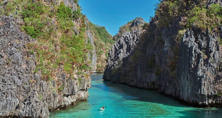 Kajakker in een serene turquoise waterweg omringd door steile rotsige kliffen.
