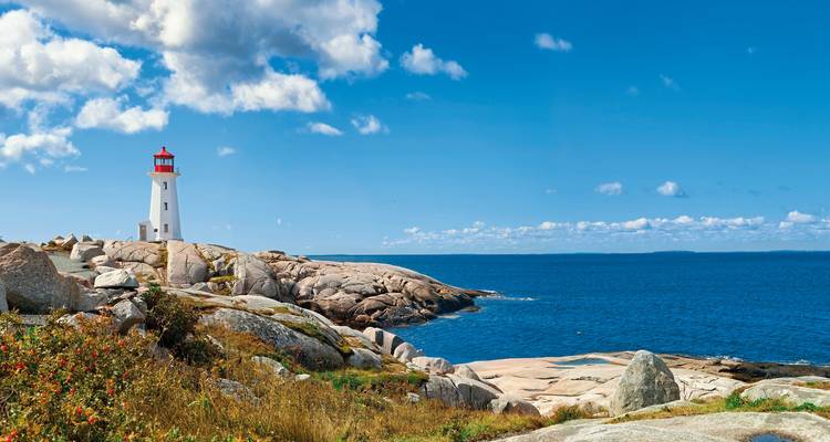 Lighthouse on rocky coastline under a bright blue sky.