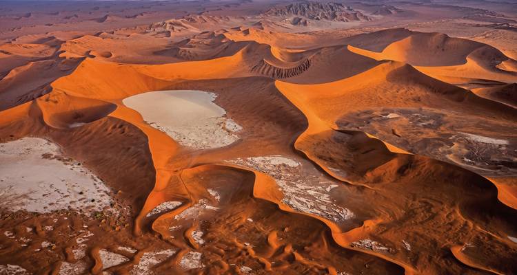 Aerial view of dramatic red sand dunes in a desert landscape.