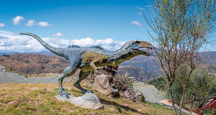 Una escultura de dinosaurio sobre un fondo de paisaje montañoso en un parque.