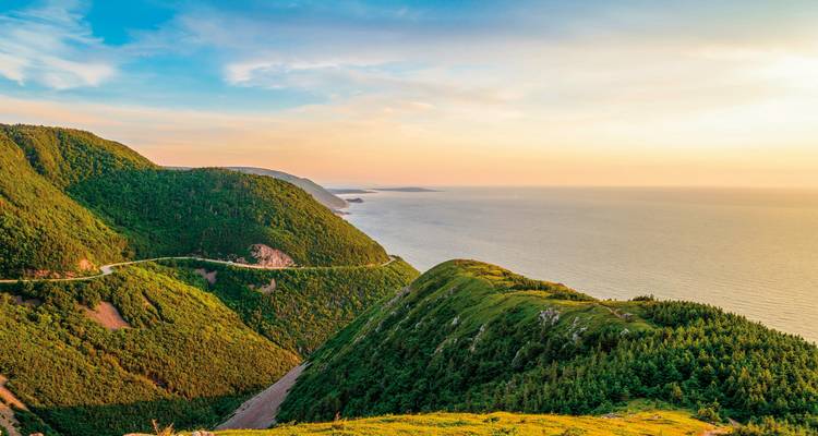 Scenic coastal road along green hills at sunset.