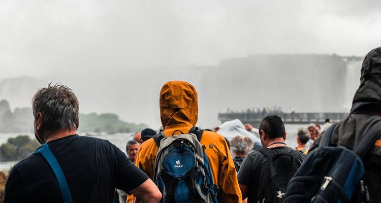 Menschen in Regenmänteln betrachten Wasserfälle mit Nebel im Hintergrund.