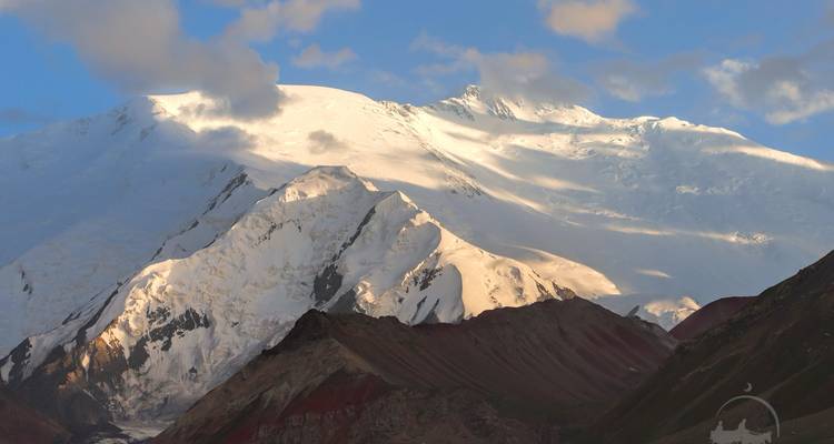 Montagnes enneigées avec un éclairage dramatique et des nuages.