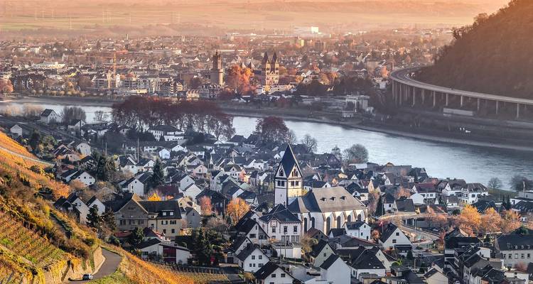 Vue panoramique d'une ville le long d'une rivière avec des collines au loin.