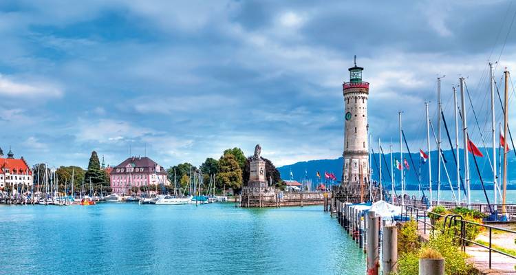 Vista pintoresca del faro de Lindau y la entrada del puerto con barcos en un día soleado.