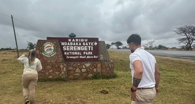 People near Serengeti National Park entrance sign.