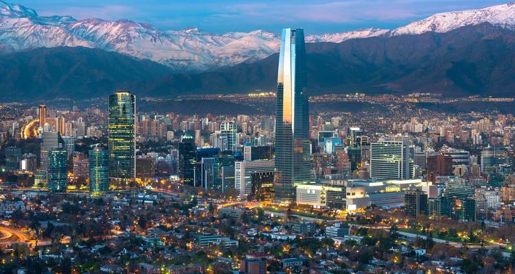 Santiago cityscape with lit-up buildings and snow-capped mountains at dusk.