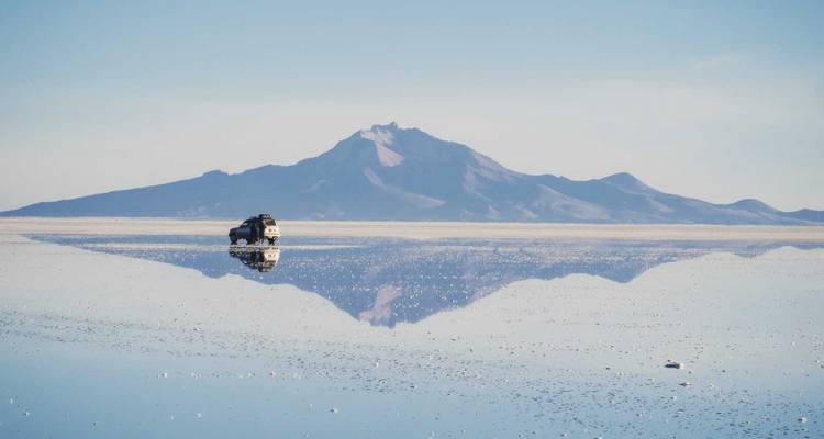 A vehicle on the reflective surface of a salt flat with a mountain in the background.