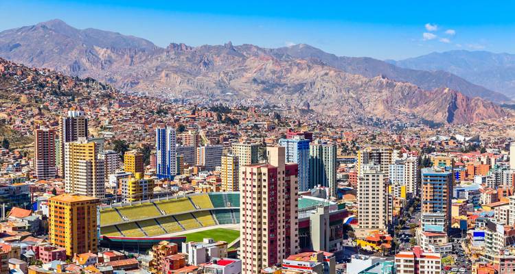 Overview of a city with modern buildings surrounded by mountains.