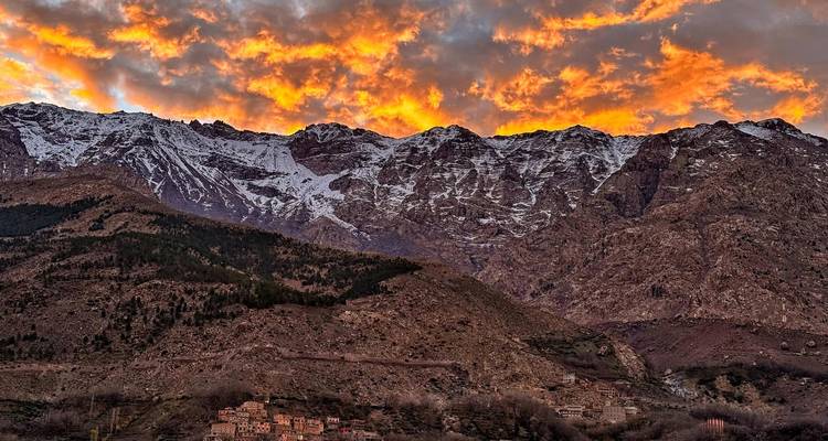 Cordillera con cimas nevadas bajo un cielo naranja dramático.