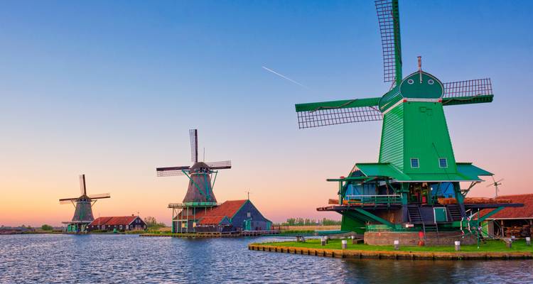 Moulins à vent au bord de l'eau sous un ciel de coucher de soleil.