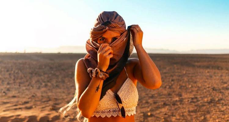 Woman in desert with covered face and sunset light.