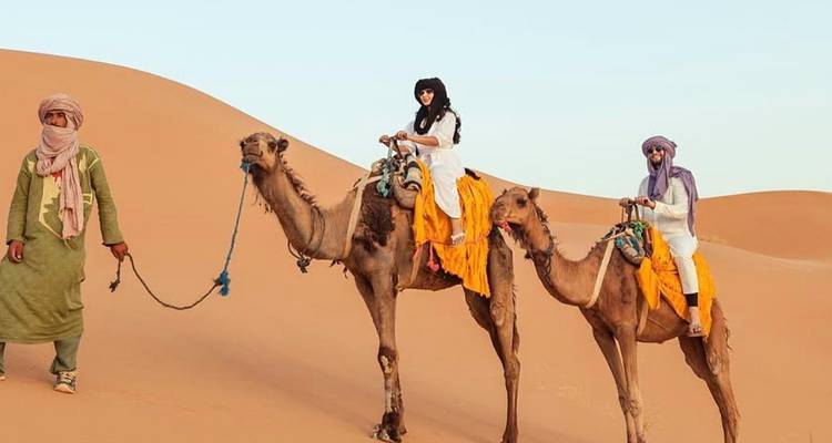 People riding camels led by a guide in the desert.