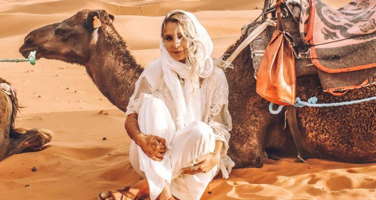 Woman sitting next to a camel in the desert.