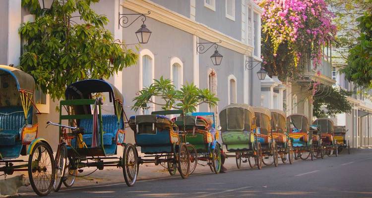 Row of traditional cycle rickshaws lined up on a quiet street.
