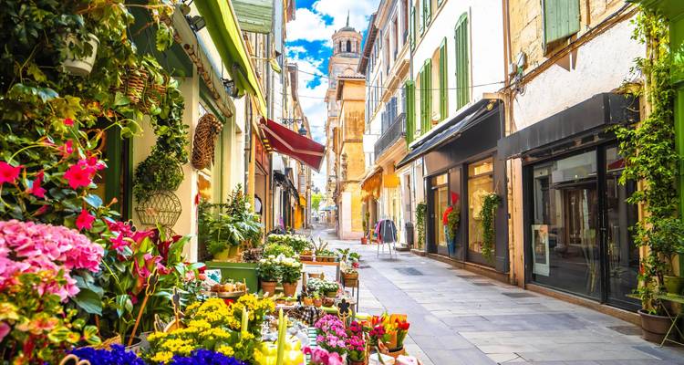 Une charmante ruelle européenne étroite bordée de magasins de fleurs et de volets colorés mène à une tour en pierre.