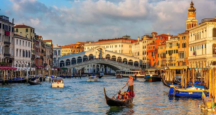 Escena icónica del Gran Canal de Venecia con góndola y el Puente de Rialto iluminados por la cálida luz del atardecer