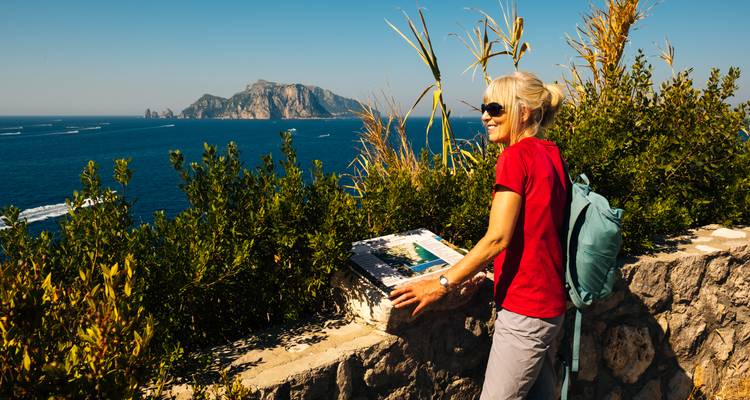 Femme profitant d'une vue sur la mer avec des falaises au loin.
