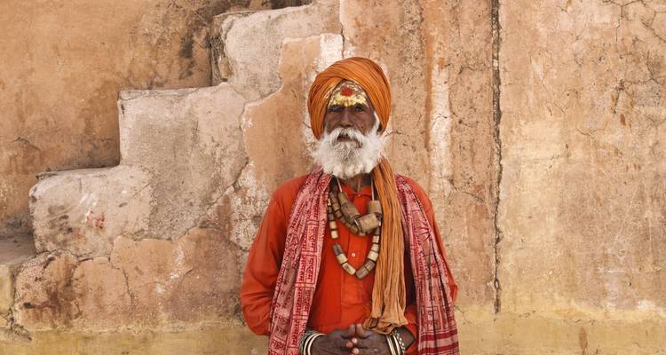 Un retrato de un hombre indio tradicional con un atuendo vibrante contra una pared antigua.