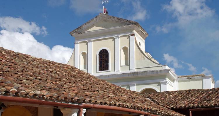 Roof of an old colonial building against a bright blue sky with clouds.